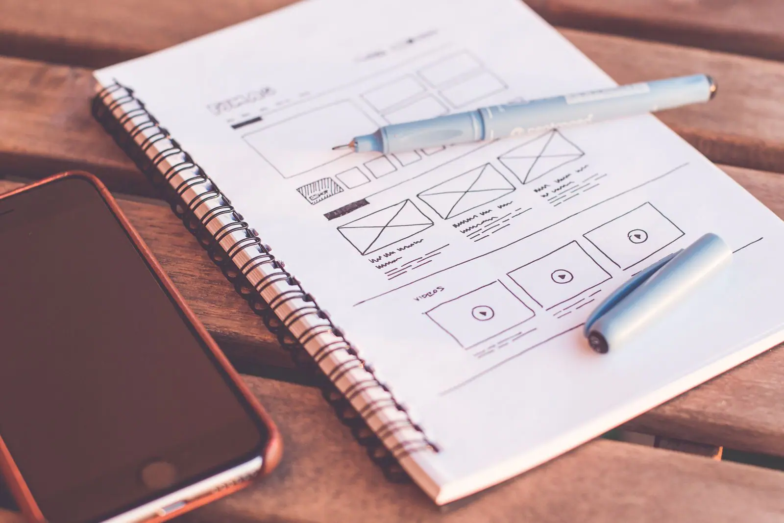 Website wireframes sketched in a notebook beside a phone and pen