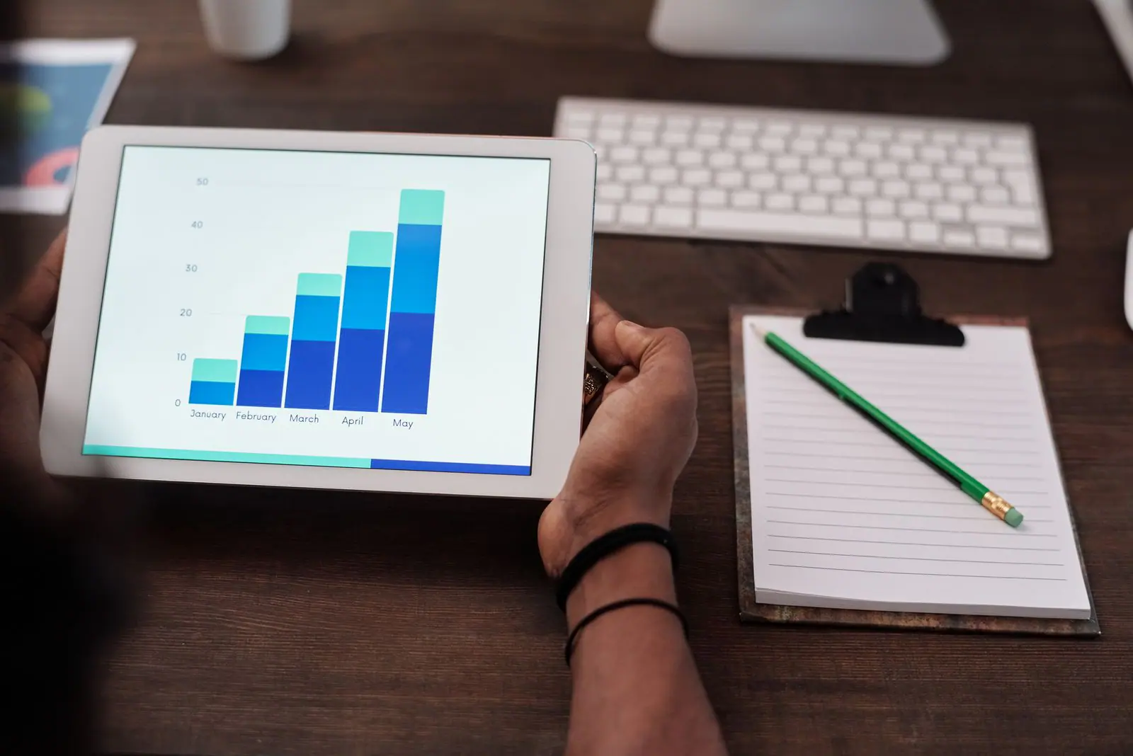 Hands holding a tablet showing a bar chart above a clipboard