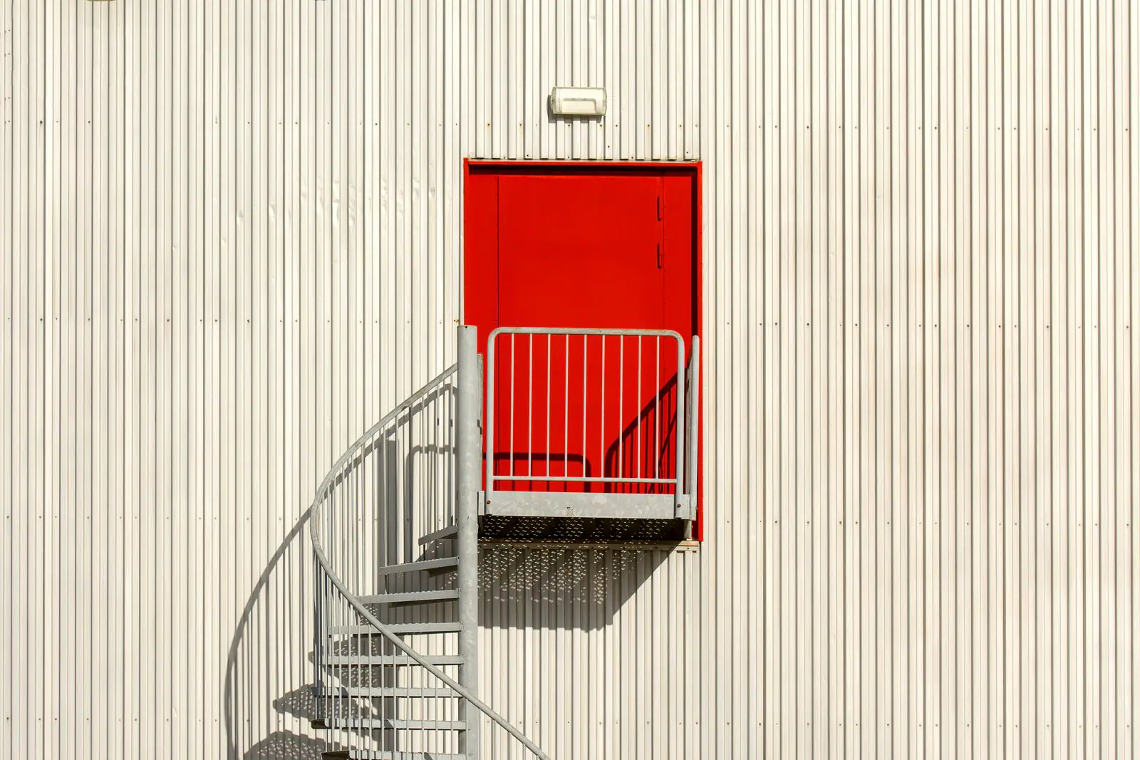 Red door at the top of a spiral staircase on a white wall
